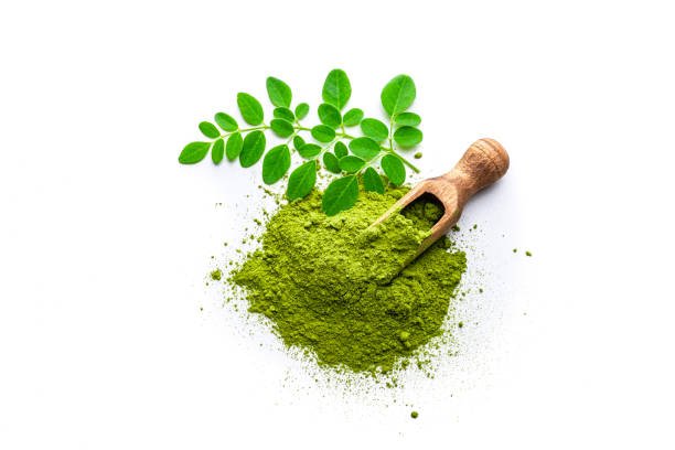 Overhead view of Matcha tea powder heap and Moringa leaves isolated on white background. A wooden serving scoop complete the composition. High resolution 42Mp studio digital capture taken with Sony A7rII and Sony FE 90mm f2.8 macro G OSS lens